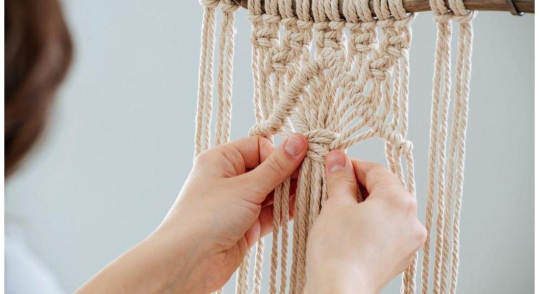 A young woman happily knotting a macramé piece while focusing intently on her work.