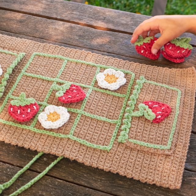 Finished crochet tic tac toe game board with pockets, featuring handmade strawberry and flower game pieces.